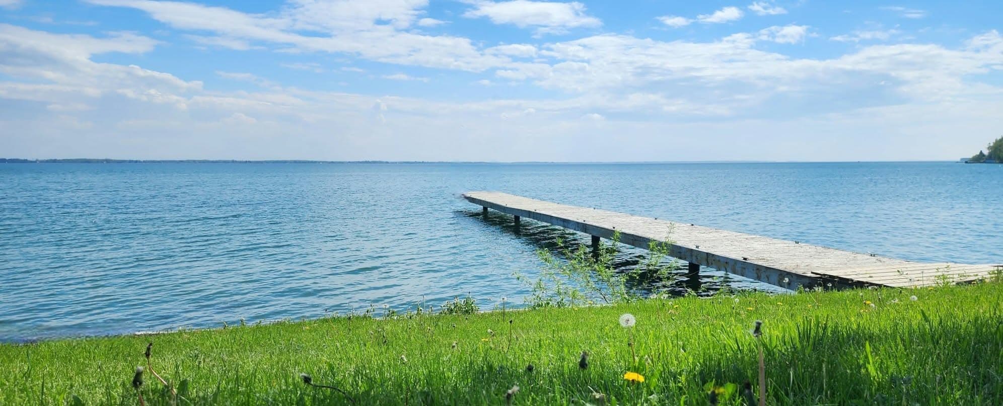 Un quai en bois s'avance sur un lac bleu calme sous un ciel nuageux.