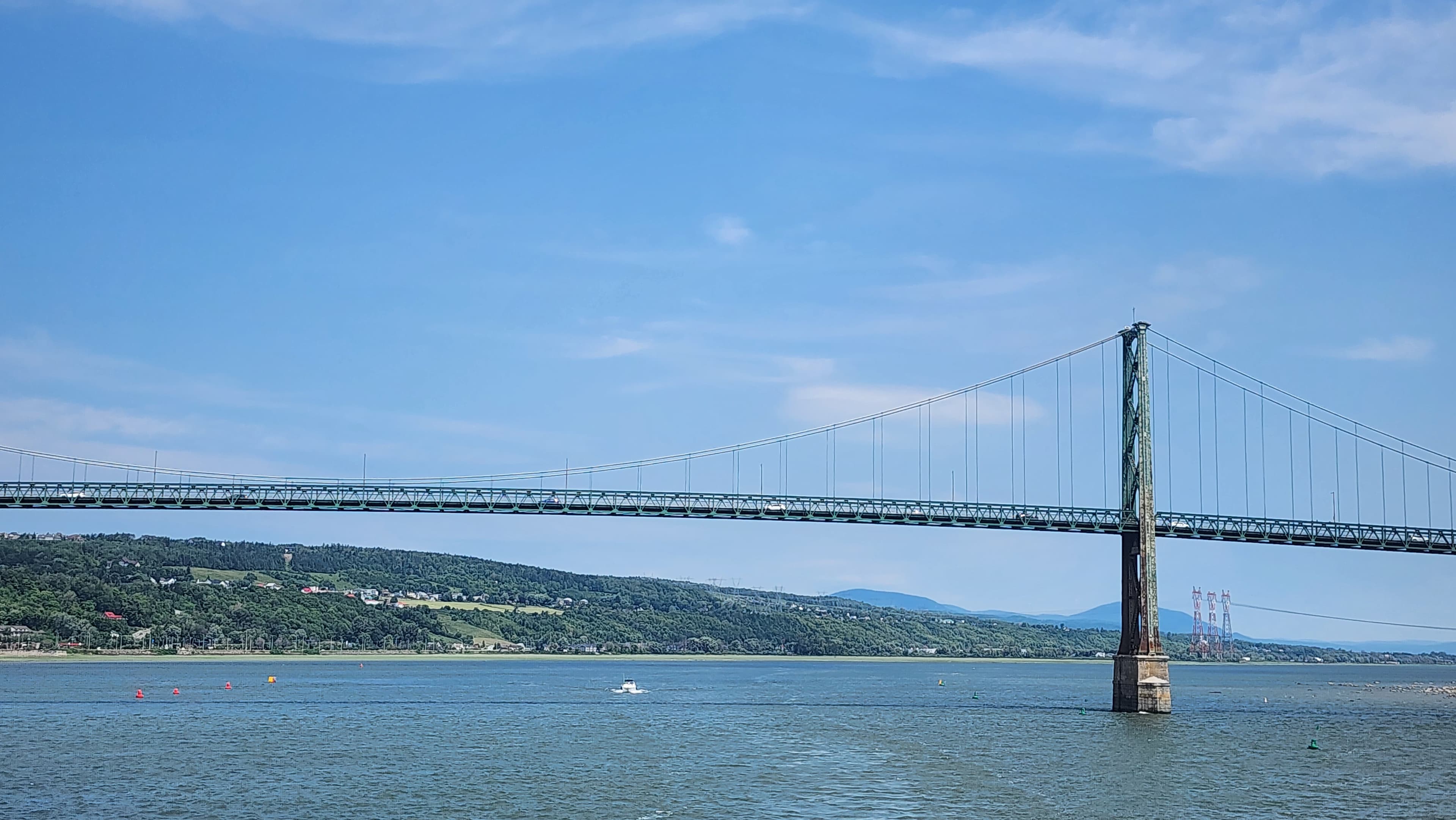 Pont suspendu surplombant un fleuve devant des collines verdoyantes sous un ciel bleu clair.