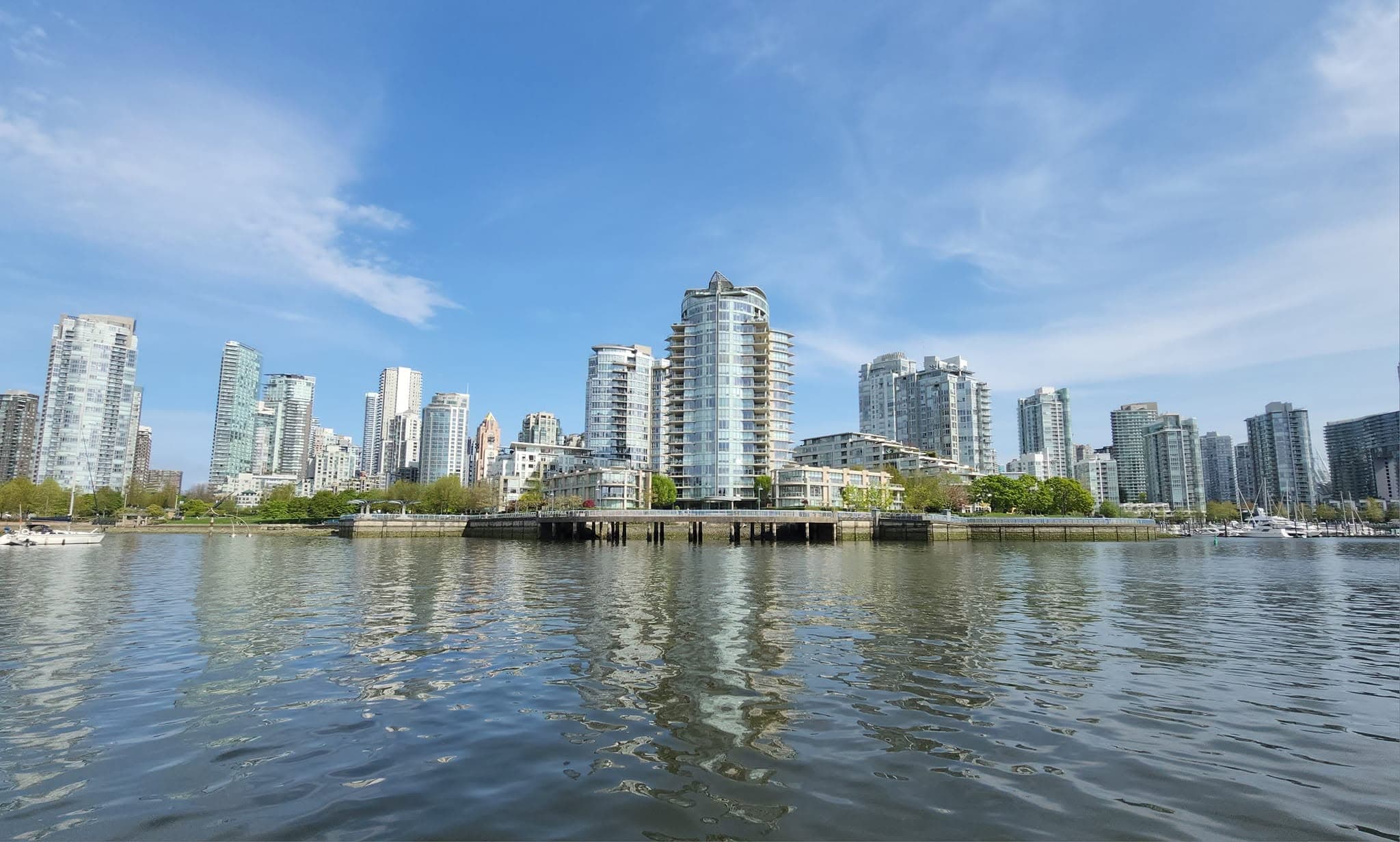 Gratte-ciel modernes se reflétant dans l'eau calme d'un port urbain sous un ciel bleu.