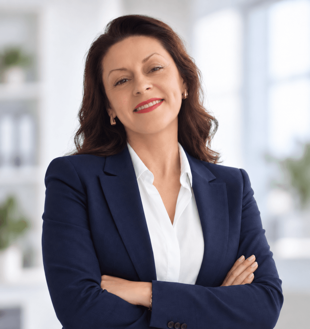 Femme d'affaires souriante en blazer bleu marine, bras croisés, dans un bureau lumineux.